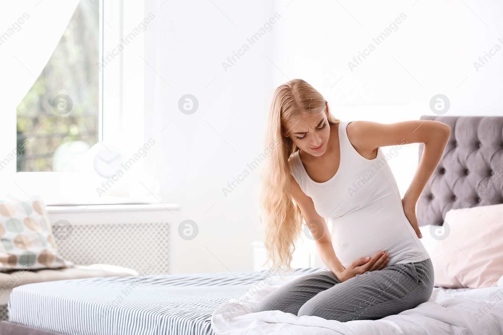 Photo of Young pregnant woman suffering from pain in bedroom. Gynecology concept