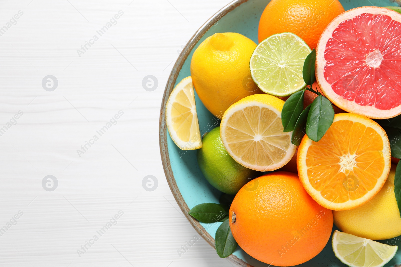 Photo of Different cut and whole citrus fruits on white wooden table, top view. Space for text