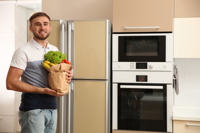 Photo of Young man with fresh food in paper bag near refrigerator at home