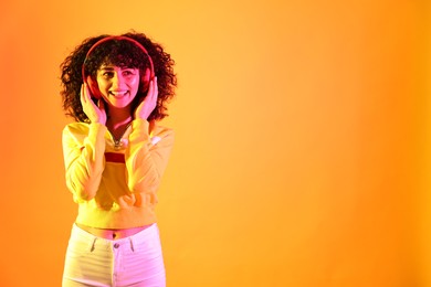 Photo of Beautiful young woman listening to music with headphones on color background in neon lights. Space for text