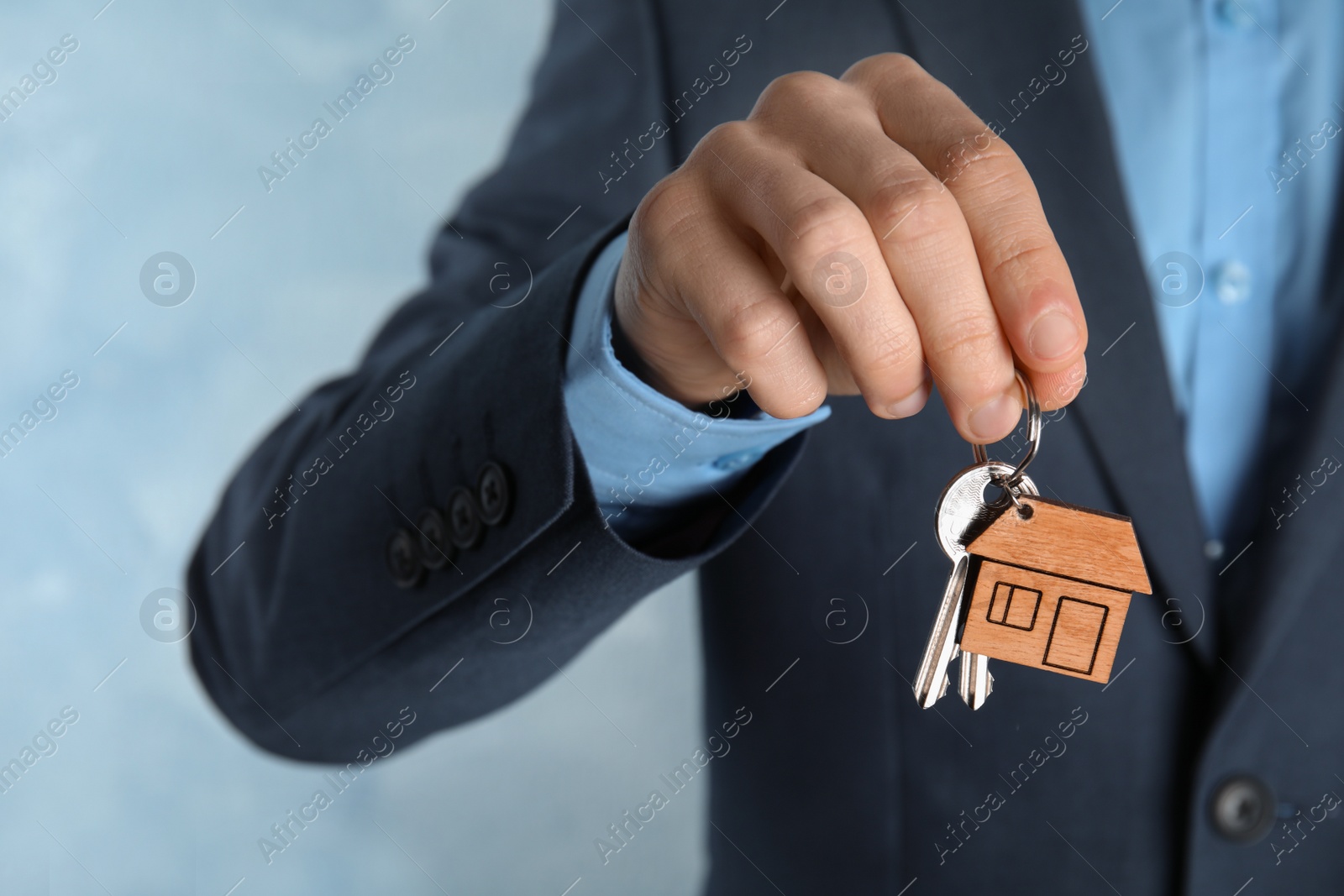 Photo of Young man holding house key with trinket on color background, closeup