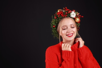 Beautiful young woman wearing Christmas wreath on black background. Space for text