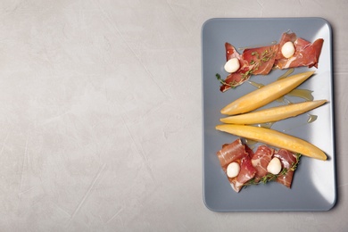 Plate of melon slices, mozzarella and prosciutto on gray background, top view. Space for text