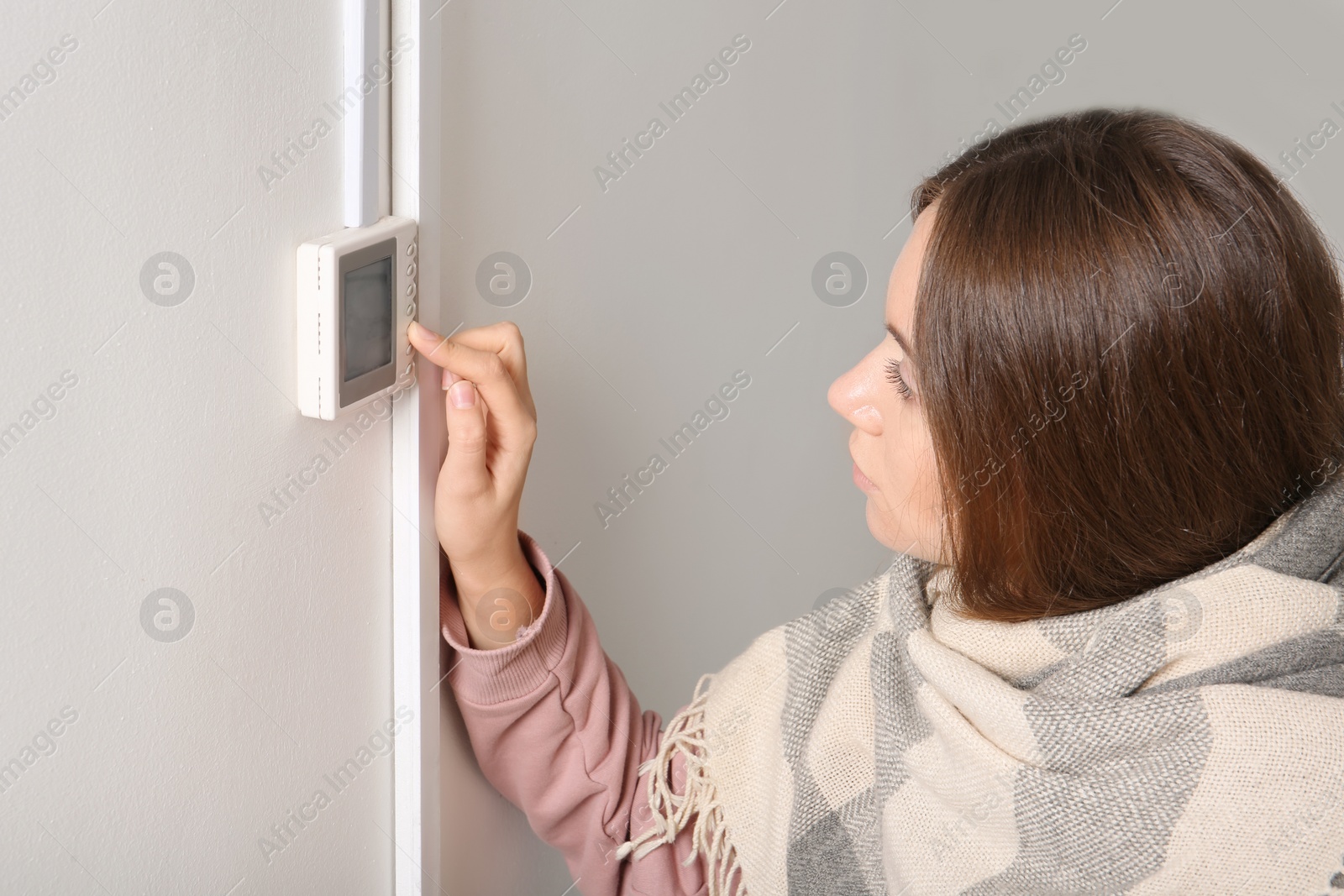 Photo of Woman adjusting thermostat on white wall. Heating system