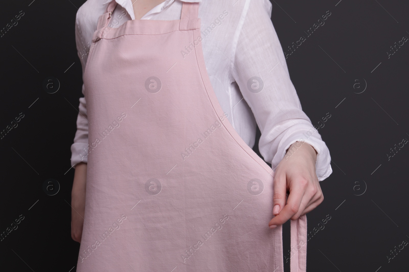 Photo of Woman putting on pink apron against grey background, closeup