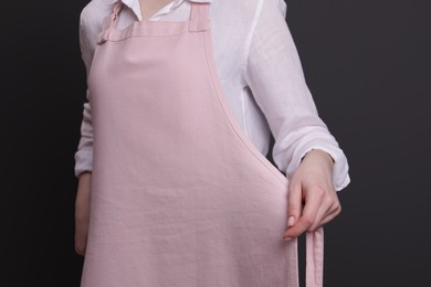 Photo of Woman putting on pink apron against grey background, closeup