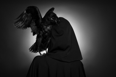 Mysterious witch with raven on dark background, back view. Black and white effect