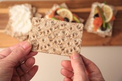 Photo of Woman holding fresh crunchy crispbread above table, closeup