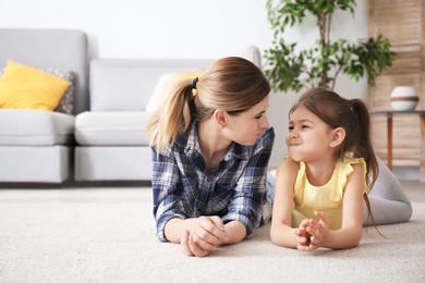 Cute little girl and her mother lying on cozy carpet at home