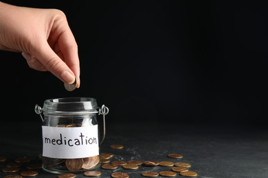 Photo of Woman putting coin into glass jar with tag MEDICATION on black table, closeup. Space for text