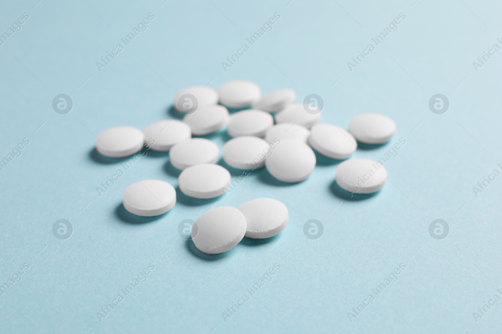 Photo of Many white pills on light blue background, closeup