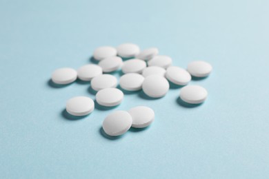 Many white pills on light blue background, closeup