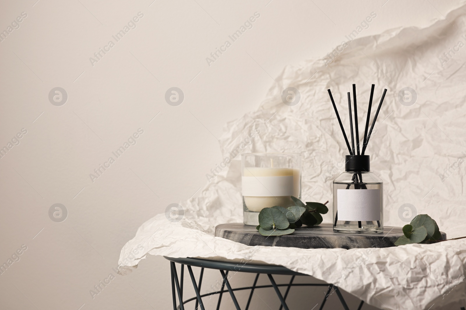 Photo of Aromatic reed air freshener, eucalyptus leaves and candle on table, space for text