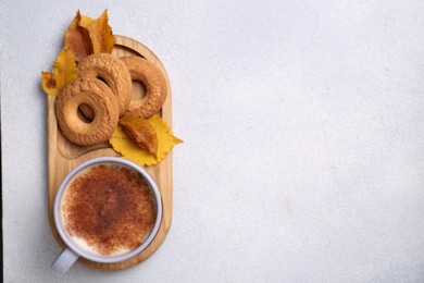 Photo of Cup of hot drink, cookies and autumn leaves on light grey textured table, top view. Space for text