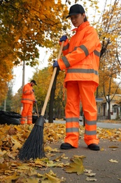 Street cleaners sweeping fallen leaves outdoors on autumn day