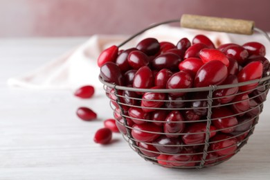 Photo of Fresh ripe dogwood berries in metal basket on white wooden table. Space for text