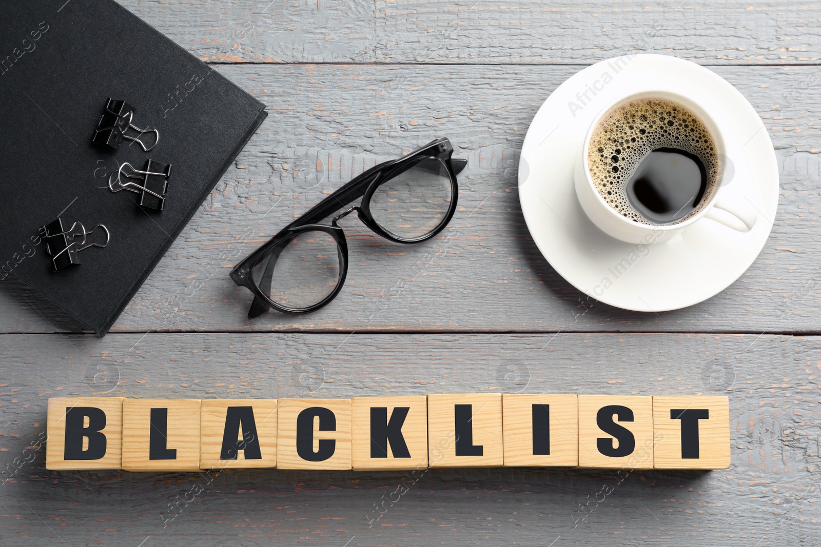 Photo of Cubes with word Blacklist, cup of coffee and office stationery on grey wooden table, flat lay