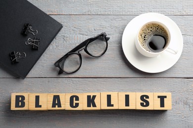 Cubes with word Blacklist, cup of coffee and office stationery on grey wooden table, flat lay