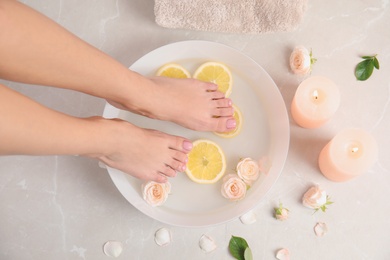 Photo of Woman putting her feet into bowl with water, roses and lemon slices on floor, top view. Spa treatment