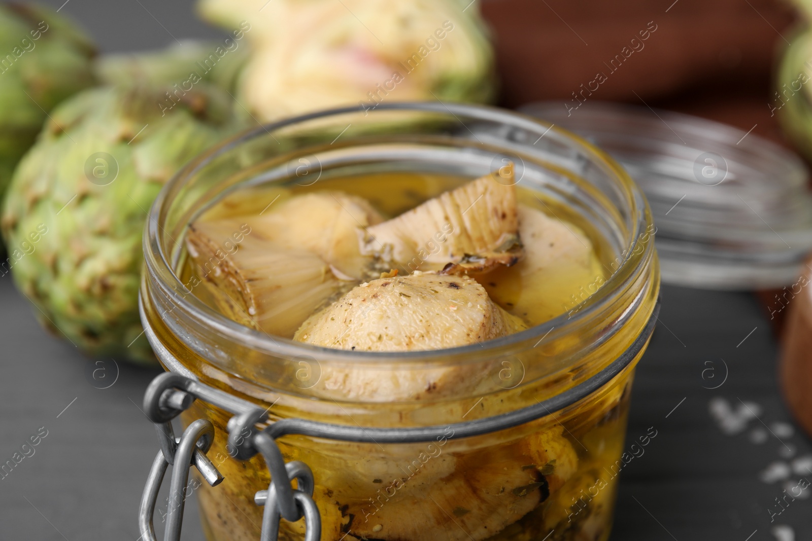 Photo of Jar of delicious artichokes pickled in olive oil on table, closeup