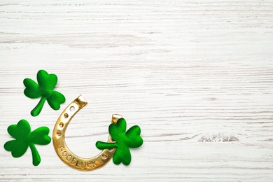 Photo of Golden horseshoe and decorative clover leaves on white wooden table, flat lay with space for text. Saint Patrick's Day celebration