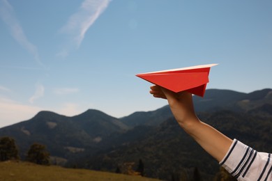 Woman with red paper plane in mountains on sunny day, closeup. Space for text