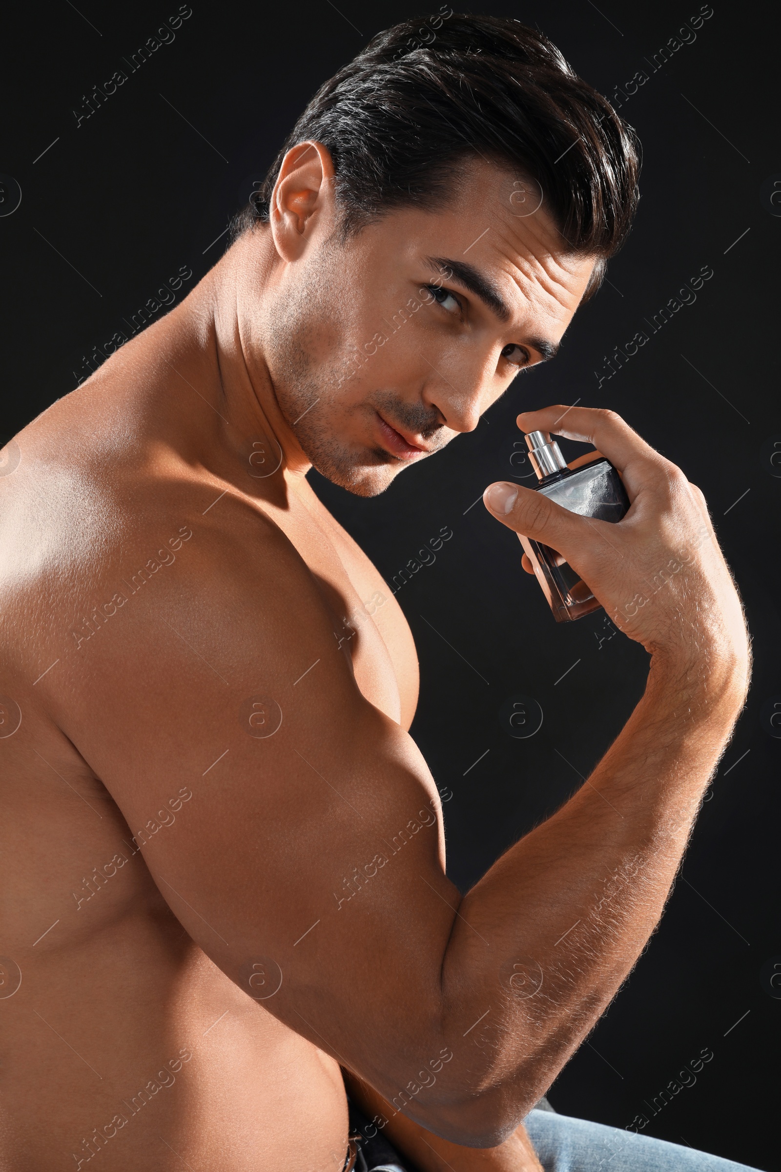 Photo of Handsome young man using perfume on black background