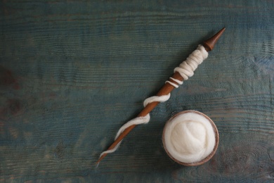 Photo of Soft white wool and spindle on blue wooden table, flat lay. Space for text