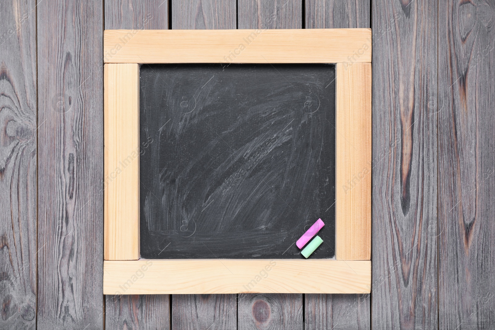 Photo of Blackboard with pieces of color chalk on wooden background, top view. Space for text