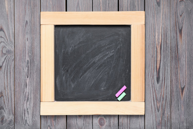 Photo of Blackboard with pieces of color chalk on wooden background, top view. Space for text