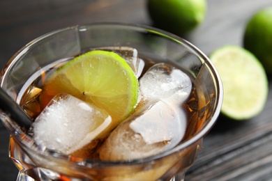 Photo of Glass of cocktail with cola, ice and cut lime on table, closeup
