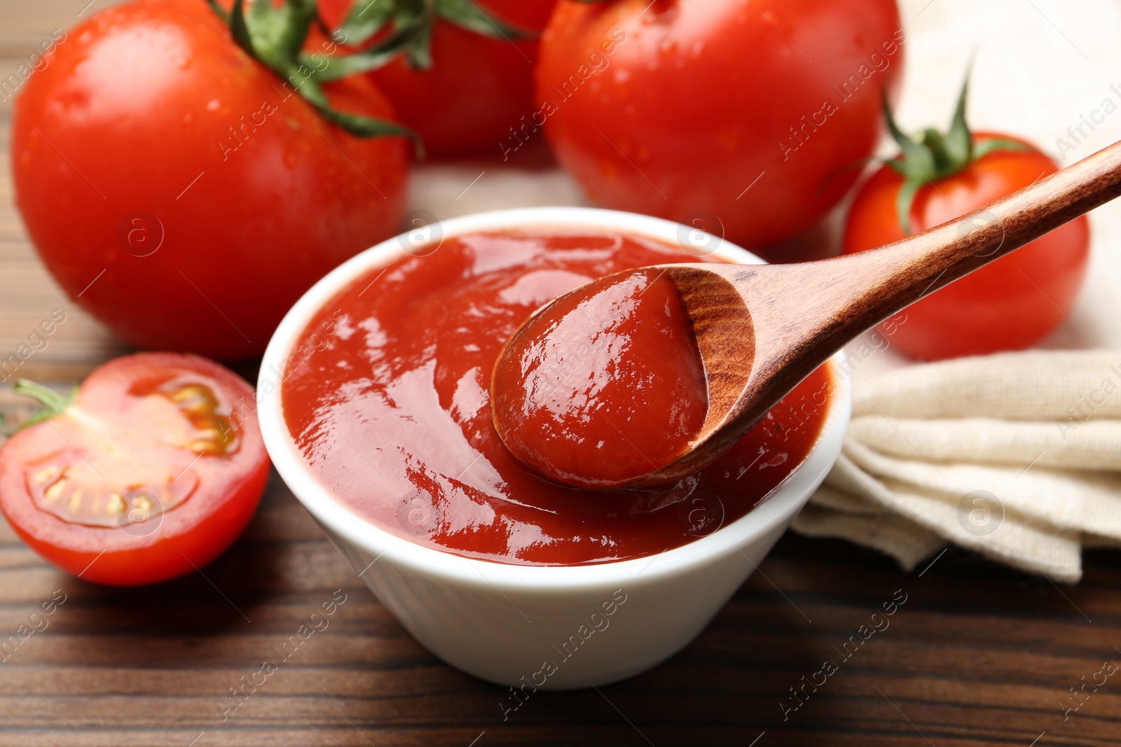 Photo of Taking delicious tomato ketchup with spoon from bowl at wooden table, closeup