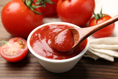 Photo of Taking delicious tomato ketchup with spoon from bowl at wooden table, closeup