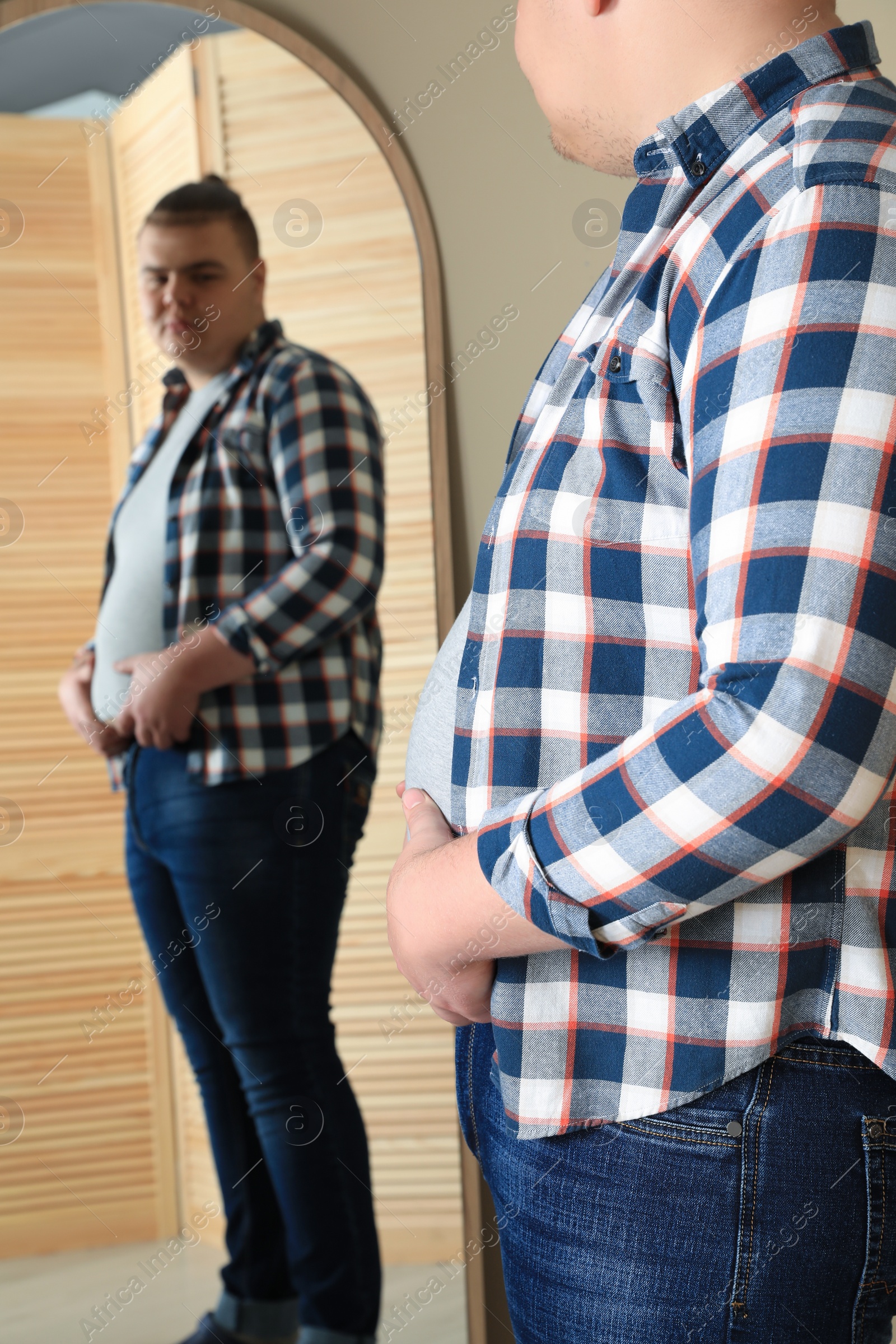 Photo of Overweight man in tight t-shirt near mirror at home