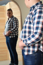 Photo of Overweight man in tight t-shirt near mirror at home