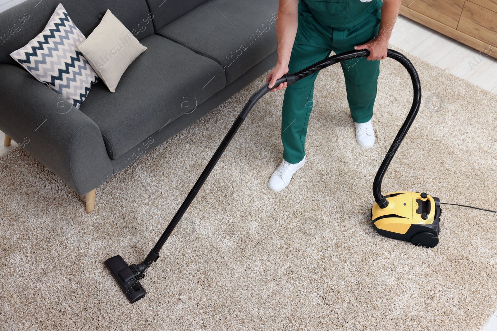 Photo of Dry cleaner's employee hoovering carpet with vacuum cleaner indoors, above view