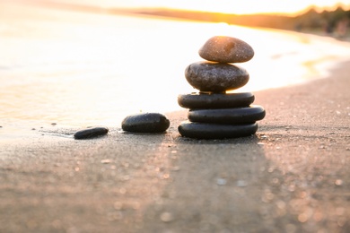 Photo of Dark stones on sand near sea at sunset, space for text. Zen concept