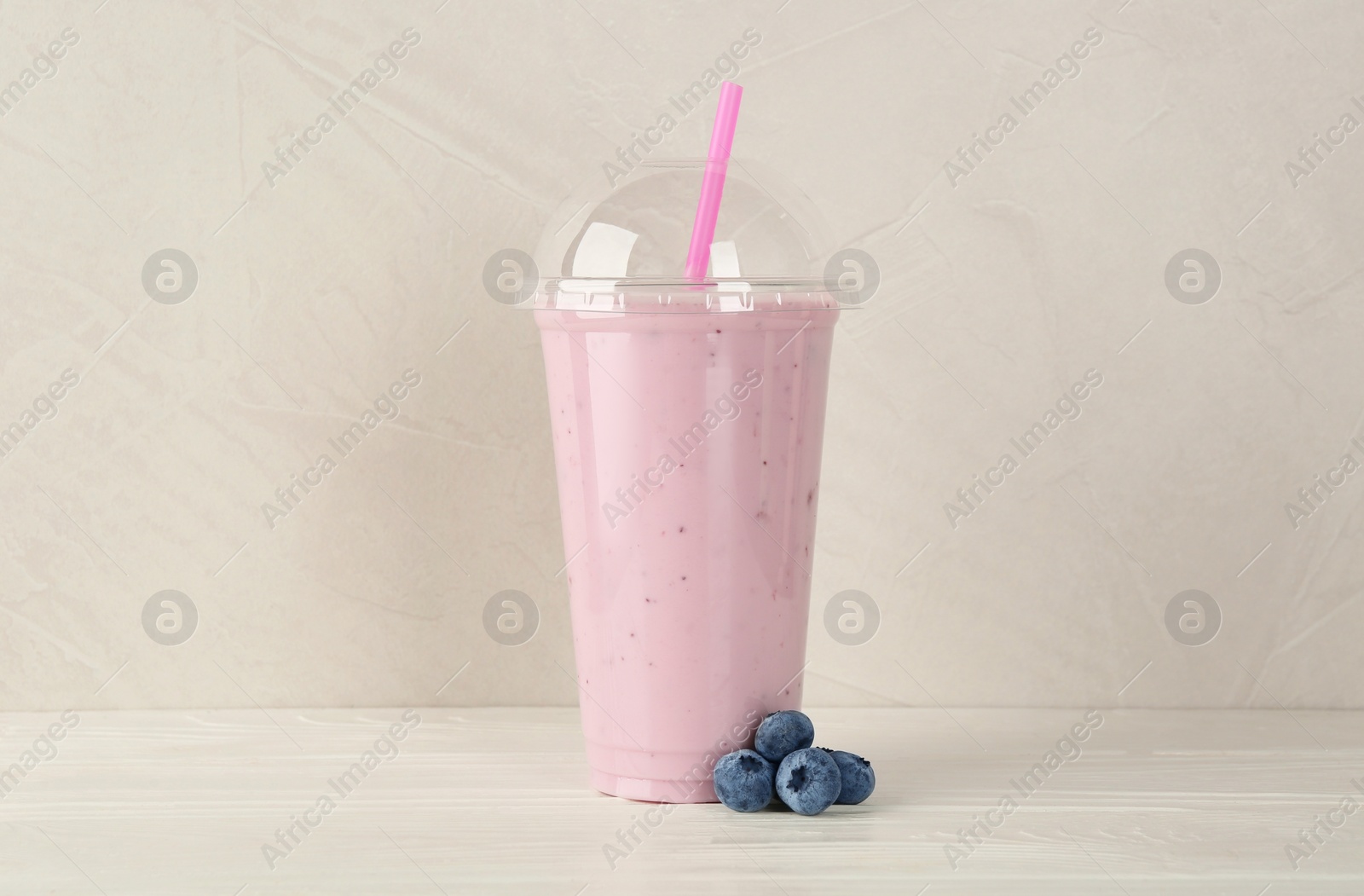 Photo of Plastic cup of tasty smoothie and fresh blueberries on white wooden table