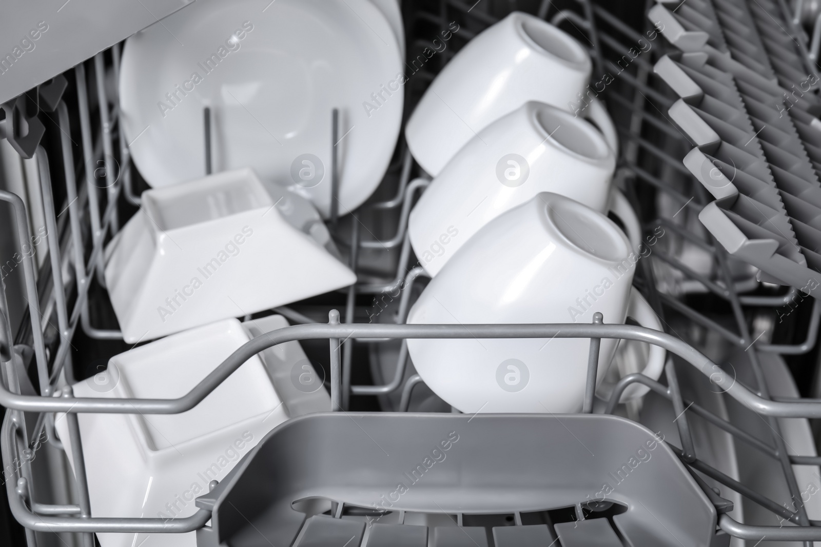 Photo of Open modern dishwasher with clean tableware, closeup