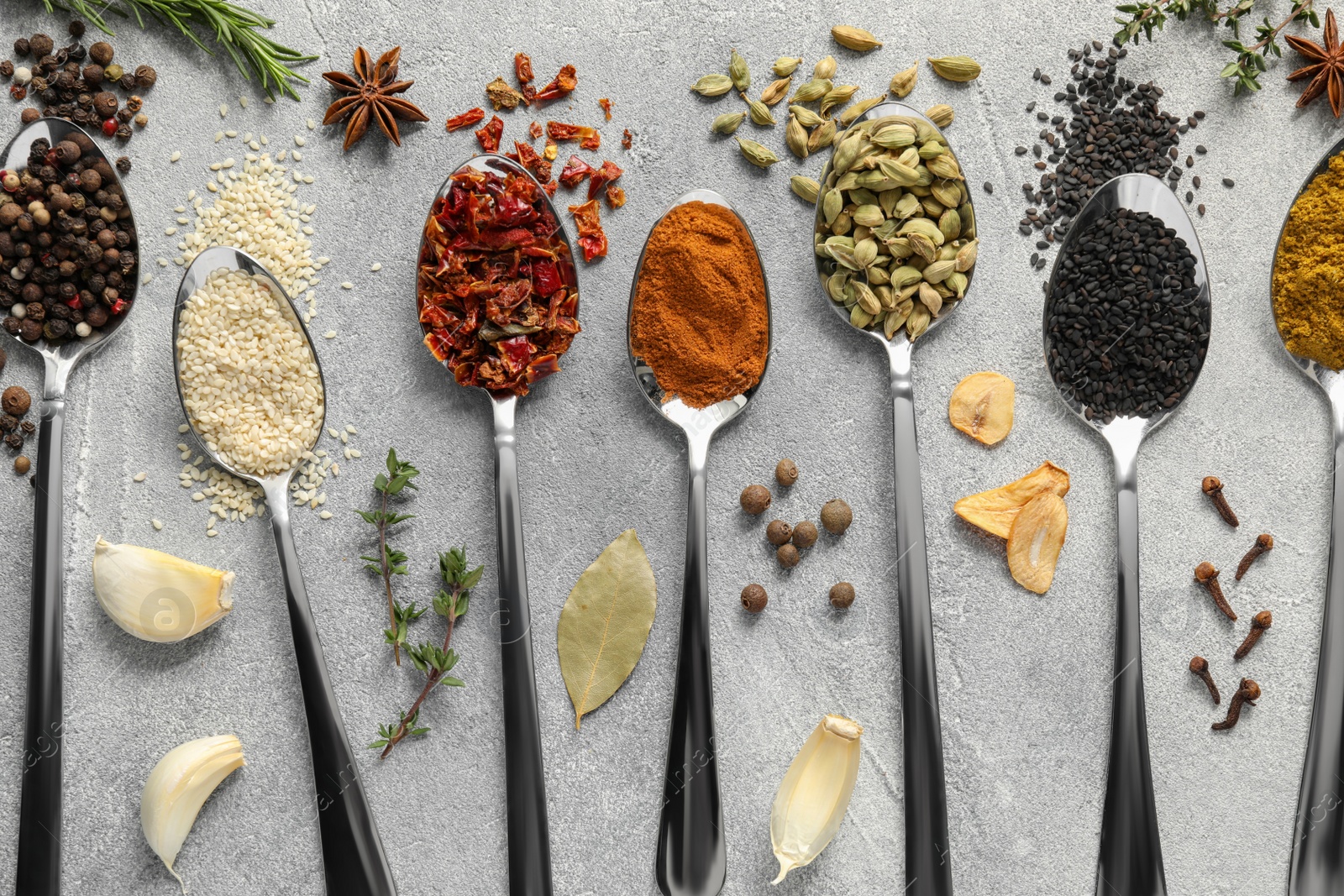 Photo of Metal spoons with different spices on light grey table, flat lay