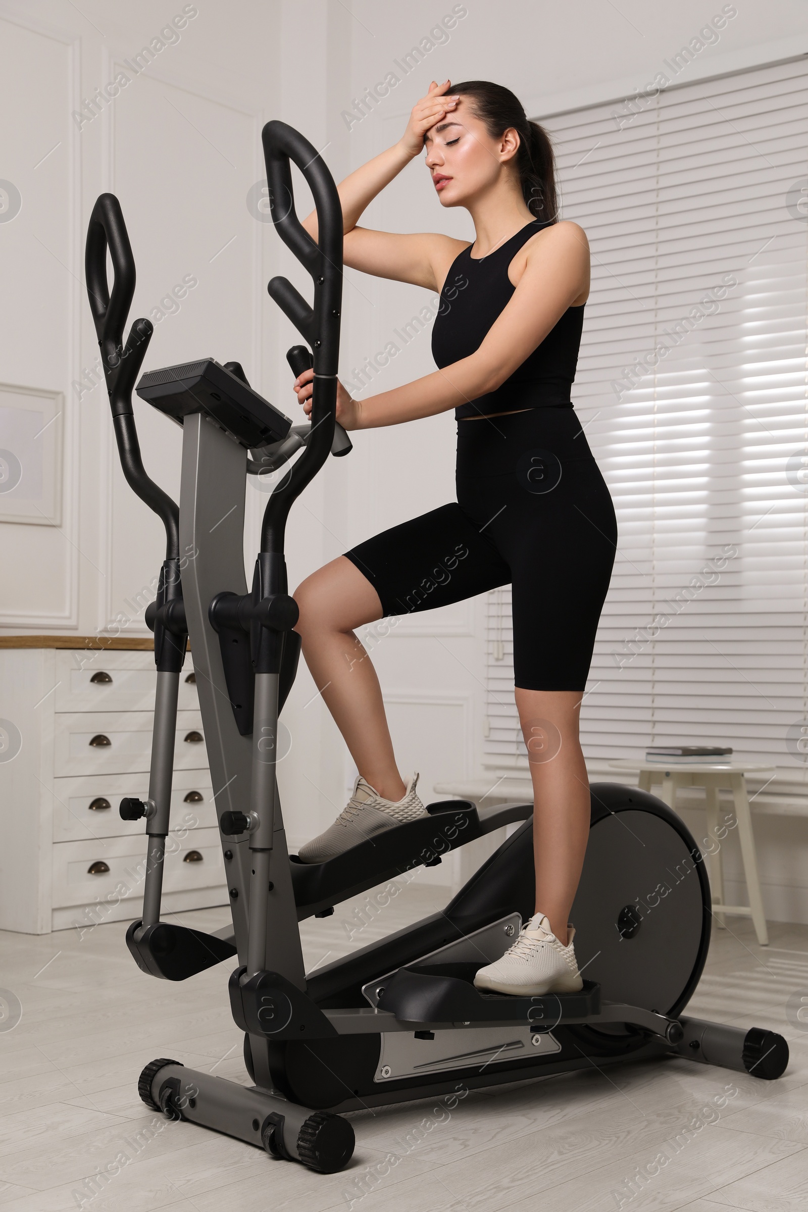 Photo of Young woman feeling tired of training on 	
elliptical machine at home