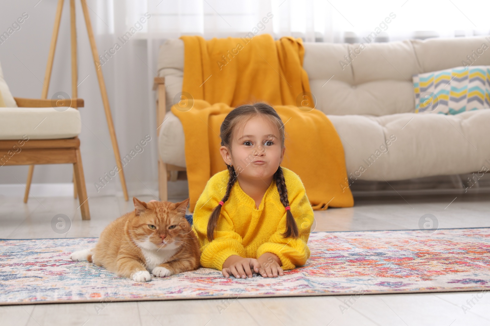 Photo of Little girl and cute ginger cat on carpet at home