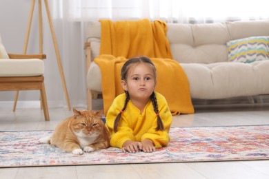 Little girl and cute ginger cat on carpet at home