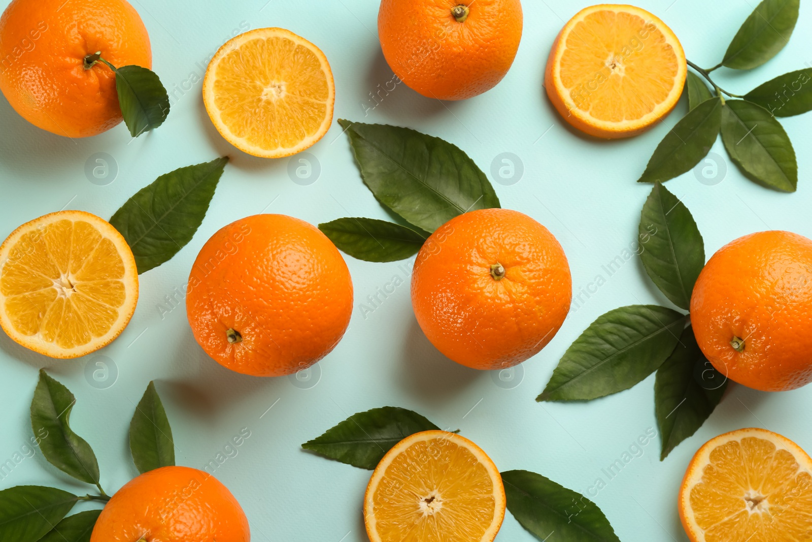 Photo of Fresh ripe oranges with green leaves on light blue background, flat lay