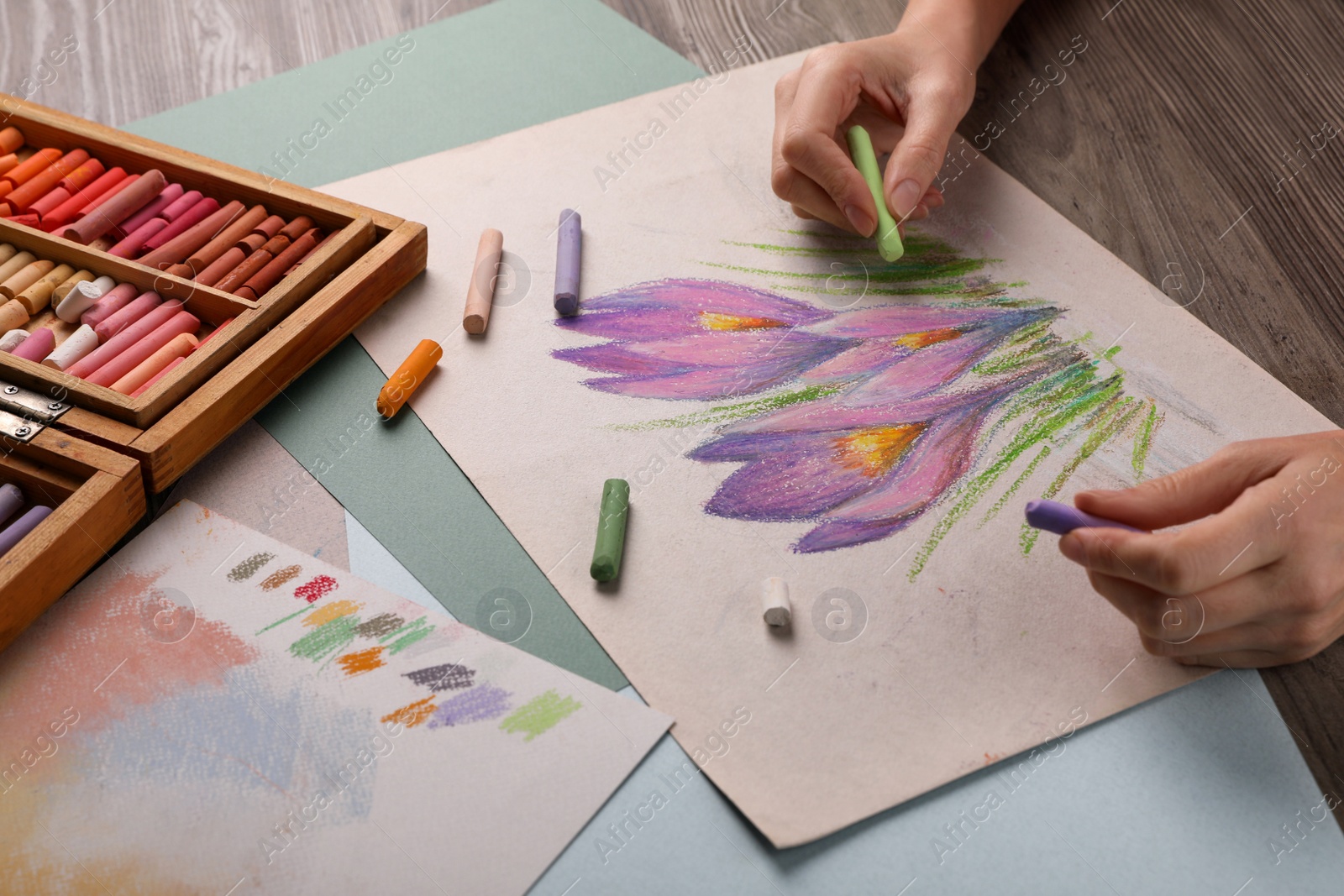 Photo of Woman drawing beautiful crocus flowers with soft pastel at wooden table, closeup