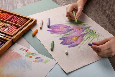 Photo of Woman drawing beautiful crocus flowers with soft pastel at wooden table, closeup