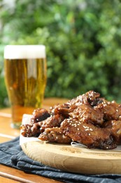 Photo of Tasty roasted chicken wings and glass of beer on wooden table, closeup