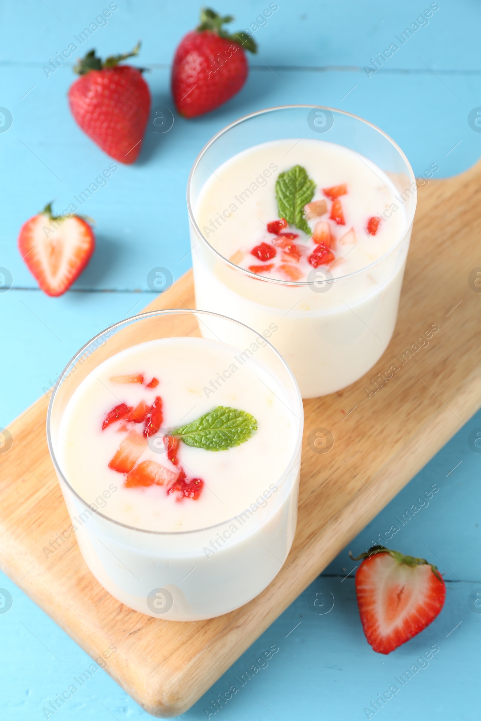 Photo of Tasty yogurt in glasses and strawberries on light blue wooden table