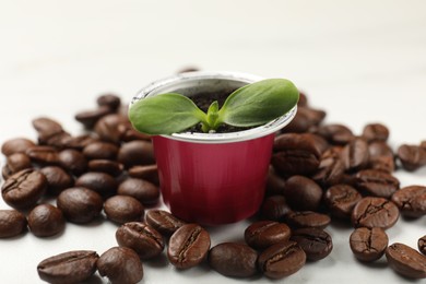 Coffee capsule with seedling and beans on white marble table, closeup