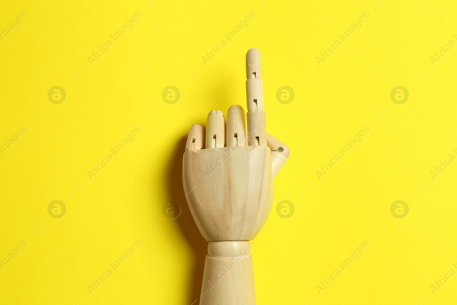 Photo of Wooden mannequin hand on yellow background, top view